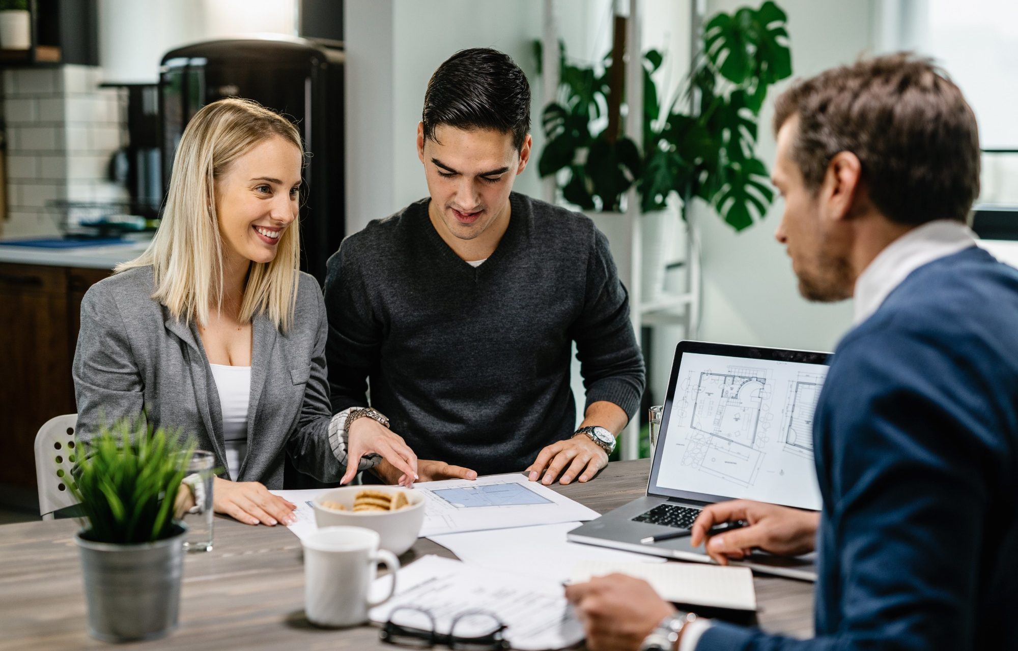 Fachberatung mit Th. Bärtle - Der Hausbau Berater - Fachberater für Fertighäuser Drei Personen besprechen Dokumente an einem Tisch in einem modernen Büroraum.