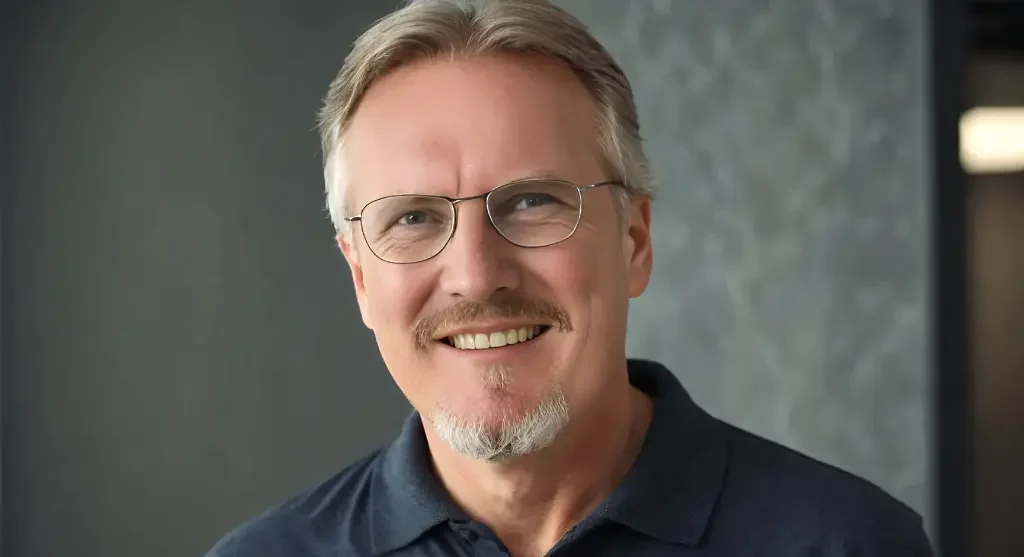 Drevo Fertigbau - Fachberater Thomas Bärtle Ein lächelnder Mann mit Brille und grauen Haaren in einem modernen Umfeld.