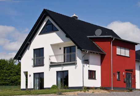 Der Hausbau Berater - Fachberater für Fertighäuser - Thomas Bärtle Modernes zweigeschossiges Haus mit schwarzem Dach, roten und weißen Wänden.