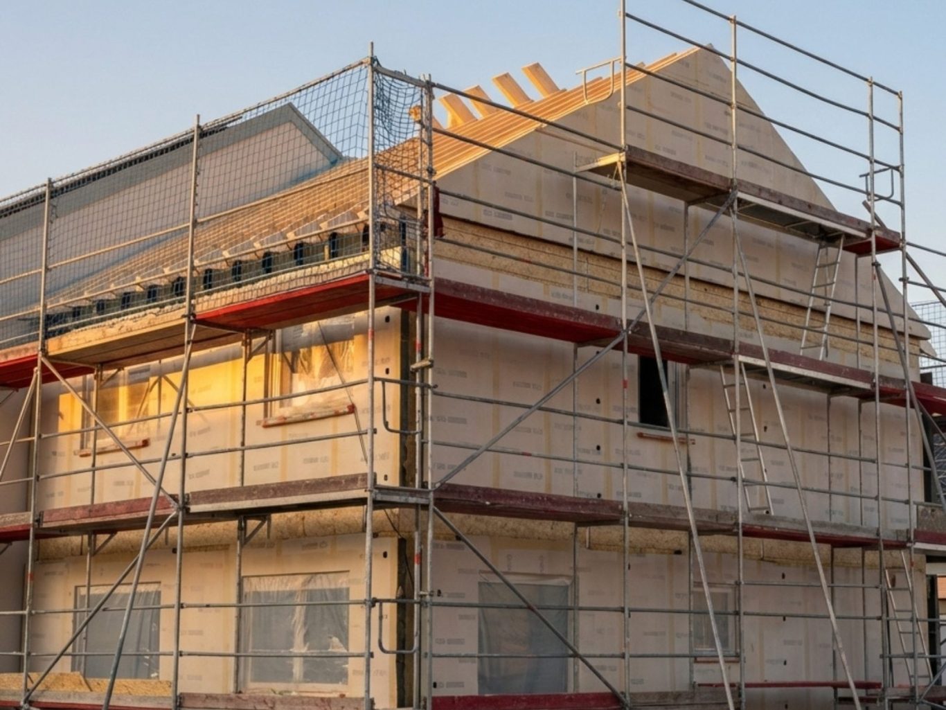 Der Hausbau Berater - Fachberater für Fertighäuser - Thomas Bärtle Gebäude mit Gerüst im Bau, Sonnenlicht fällt auf die Fassade.