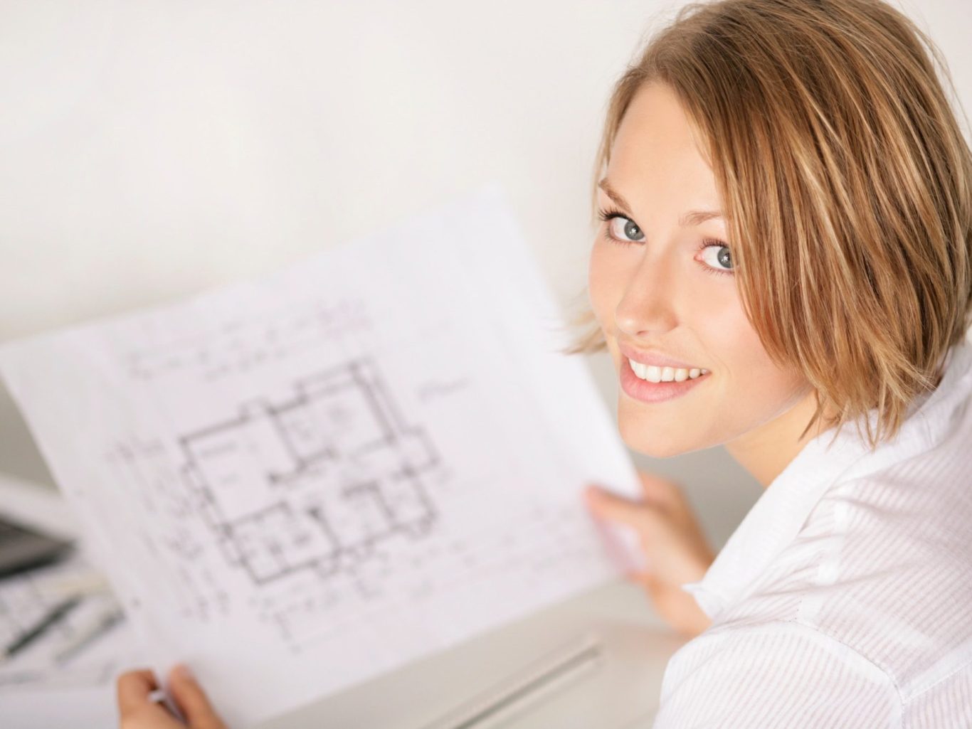 Der Hausbau Berater - Fachberater für Fertighäuser - Thomas Bärtle Junge Frau hält einen Bauplan und lächelt freundlich in die Kamera.